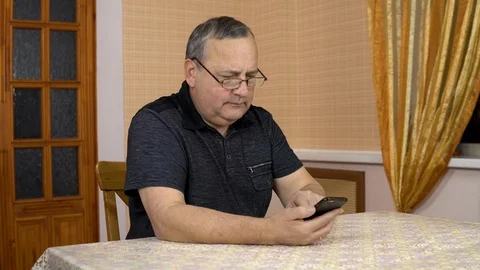 A man uses a phone with a serious face. The old man dialed the number and Stockbeeldmateriaal 124655764