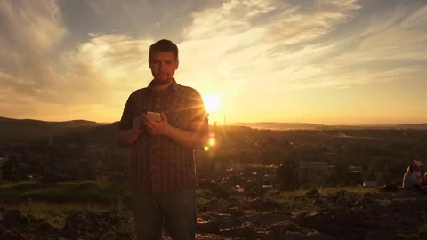 The man uses the phone standing on the hill at sunset in the summer. Stock Footage 78716358