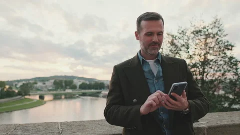Man uses phone while standing on the embankment of the river Stock Footage 227135191