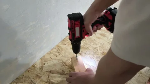 A man uses a power drill to screw a screw into a wooden board on a table. Repair Stock Footage 321390216