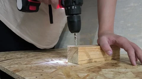 A man uses a power drill to screw a screw into a wooden board on a table. Repair Stock Footage 321390309
