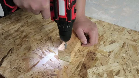 A man uses a power drill to screw a screw into a wooden board on a table. Repair Stock Footage 321390341