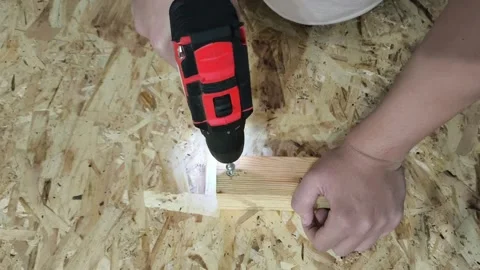 A man uses a power drill to screw a screw into a wooden board on a table. Repair Stock Footage 321390372