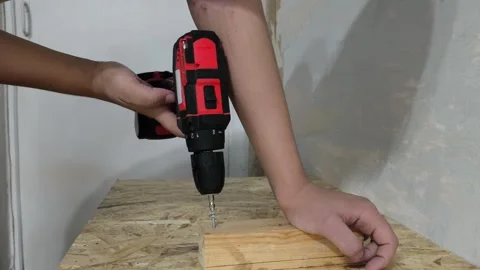 A man uses a power drill to screw a screw into a wooden board on a table. Repair Stock Footage 321390379