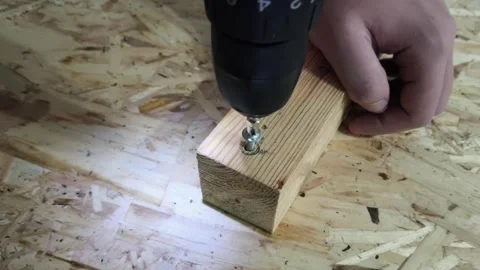 A man uses a power drill to screw a screw into a wooden board on a table. Repair Stock Footage 321390405