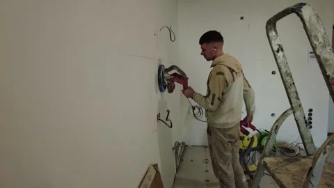 Man uses power tool to cut wall in construction site while wearing headphones Video stock 332477245