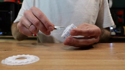 A man uses precision tweezers to remove blue PET-G support material from a Stock Footage 344301244