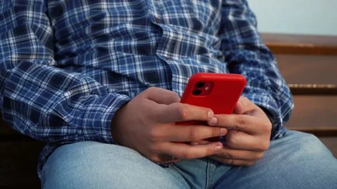 Man uses a red phone while sitting on a bench in the park. without face Stock Footage 157697580