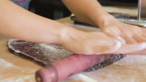 Man uses a rolling pin to flatten beet purple pasta dough sheet Stock Footage 199153232