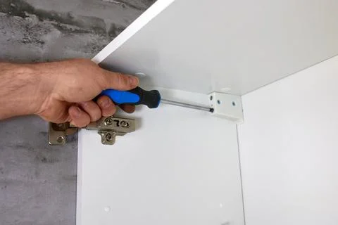 A man uses a screwdriver to fix a bracket mounted on a white rack, a cabine.. Fotos Stock