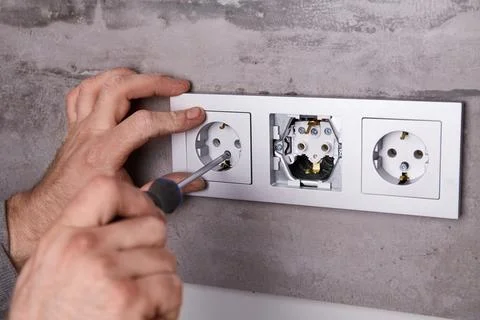 A man uses a screwdriver to install an electrical outlet on a porcelain til.. Stock Photos