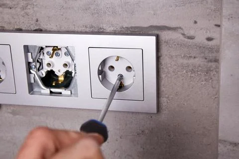 A man uses a screwdriver to install an electrical outlet on a porcelain til.. Stock Photos