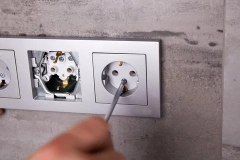 A man uses a screwdriver to install an electrical outlet on a porcelain til.. Stock Photos