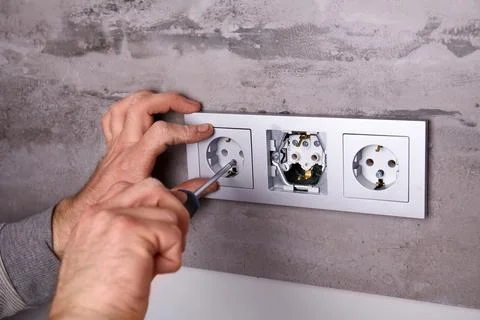 A man uses a screwdriver to install an electrical outlet on a porcelain til.. Stock Photos