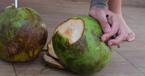 A Man Uses a Sharp Knife to Cut Open the Top of a Fresh Coconut Stock Footage 286433540