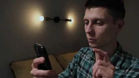 A man uses a smartphone to control smart home features in a dark bedroom at nigh Stock-Footage 296981130