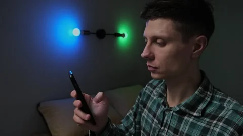 A man uses a smartphone to control smart home features in a dark bedroom at nigh Stock Footage 297189240