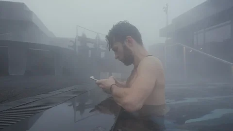 Man uses a smartphone in the geothermal pool in winter snow day Stock Footage 106215918