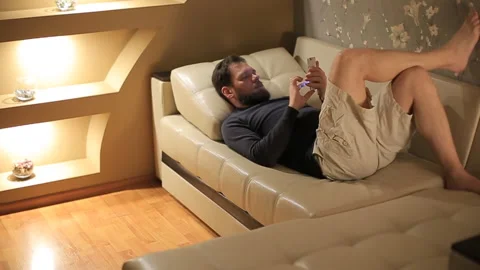 Man uses a smartphone at home on the couch in the evening Stock Footage 87312470
