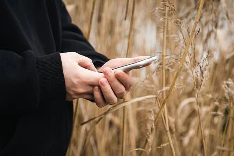 A man uses a smartphone while standing in the reeds by the river, close-up. Stock Photos