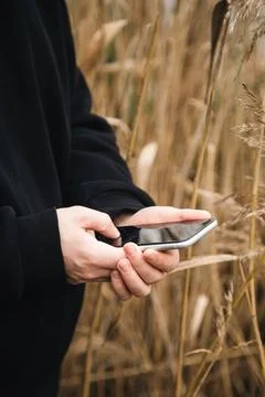 A man uses a smartphone while standing in the reeds by the river, close-up. Stock Photos