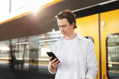 Man uses a smartphone while waiting for a train at the station platform. Th.. Stock Photos
