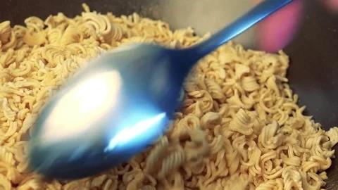 A man uses a spoon to mix instant ramen noodles with spice - closeup Stock Footage