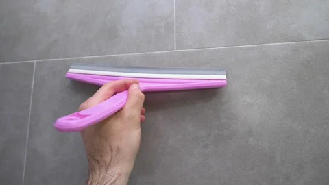 A man uses a squeegee to remove water from a bathroom tile. Stock Footage 323968643