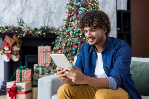 A man uses a tablet computer while sitting at home in the living room for Stock Photos