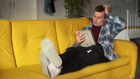 A man uses a tablet lying on the couch Stock Footage 157367875