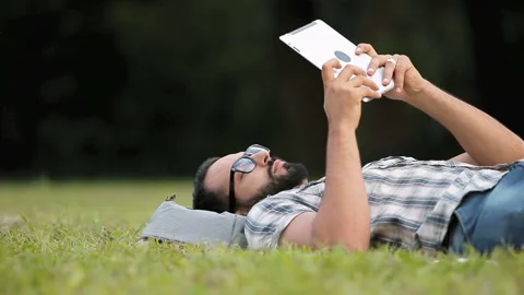 Man Uses Tablet Lying on Grass 動画素材 95721991