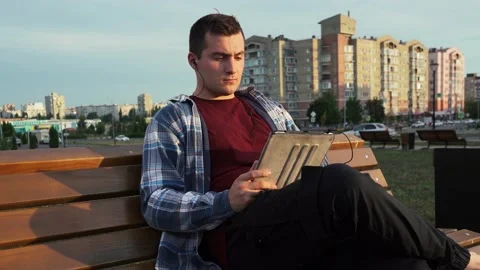 Man uses a tablet while sitting on a bench in the park Stock-Footage 157921360