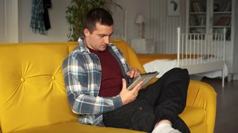 A man uses a tablet while sitting on the couch in the room Stock Footage 161658662