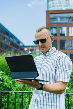 Man uses tablet while standing outdoors in a city setting with modern buildin Stock Photos