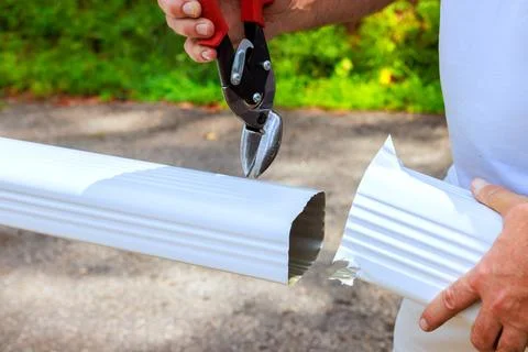 Man uses tool to cut white pipe while standing on gravel path Stock Photos