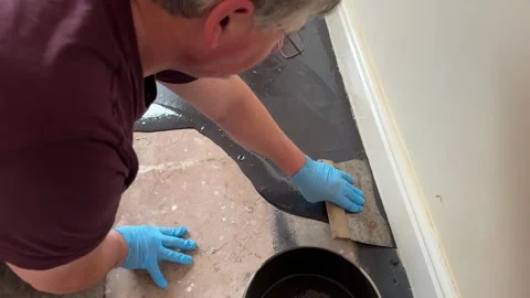 Man uses a trowel to apply damp proof membrane coating to a floor Stock Footage 292999882