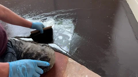 Man uses a trowel to apply damp proof membrane coating to a floor Stock Footage 292999924