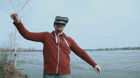 A man uses virtual reality glasses while standing next to a spring pond. Stock Footage 74966810