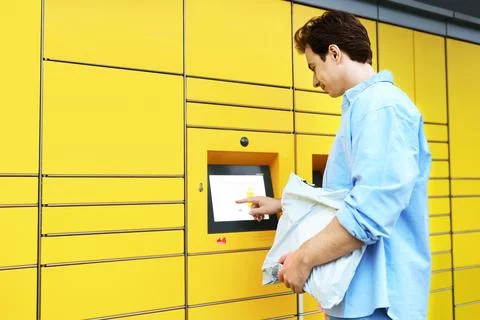 Man uses a yellow parcel locker terminal for a contactless delivery pickup... Stock Photos