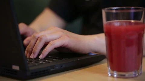 Man using and typing on a laptop by a glass of juice. Stock Footage 51709308