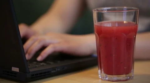 Man using and typing on a laptop by a glass of juice. Stock Footage 51709309
