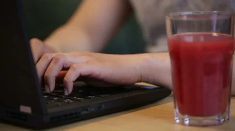 Man using and typing on a laptop by a glass of juice. Stock Footage 51709312
