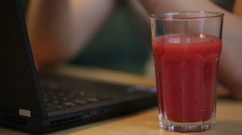 Man using and typing on a laptop by a glass of juice. Stock Footage 51709315