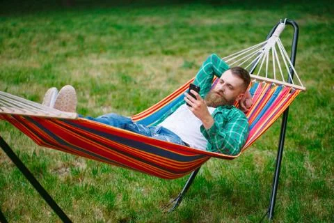 Man using an app on his mobile phone white swinging in a hammock. 스톡 사진
