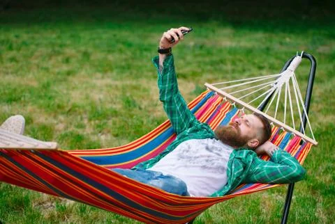 Man using an app on his mobile phone white swinging in a hammock. Stock Photos