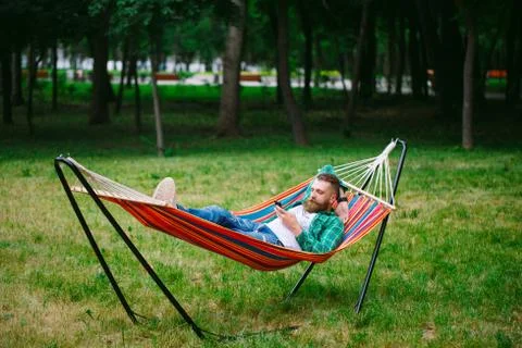 Man using an app on his mobile phone white swinging in a hammock. Stock Photos