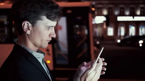 Man using app on his smartphone ordering the taxi on a urban street in evening Stock Footage 80009647