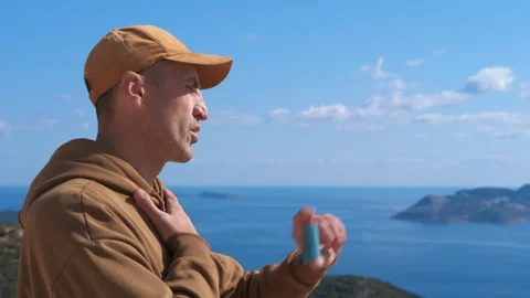 Man using asthma inhaler outdoors overlooking the sea. Stock Footage 330609612