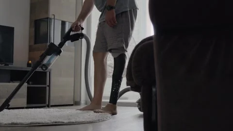 Man Using Bionic Leg to Start Vacuum Cleaner in Bright Living Room 库存影片 317899149