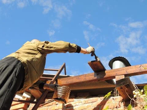 A man using a brush to paint or treat a wooden roof structure Stock Photos